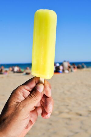 closeup of a young caucasian man with an appetizing ice pop in his hand on the beachの写真素材