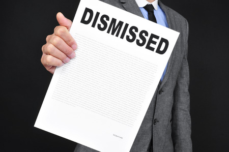 a young caucasian man in gray suit showing a document with the text dismissal written in it on a black backgroundの写真素材