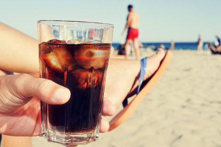 Closeup of a young caucasian man hanging out on the beach with a glass with cola drinkの写真素材