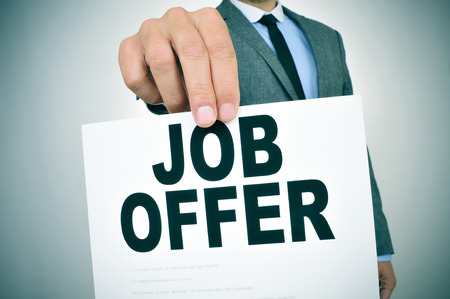 closeup of a young businessman in a grey suit shows a signboard with the text job offer written in itの写真素材