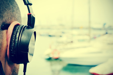 closeup of a young man listening to music with headphones in front of the sea in a marina, with a filter effectの写真素材