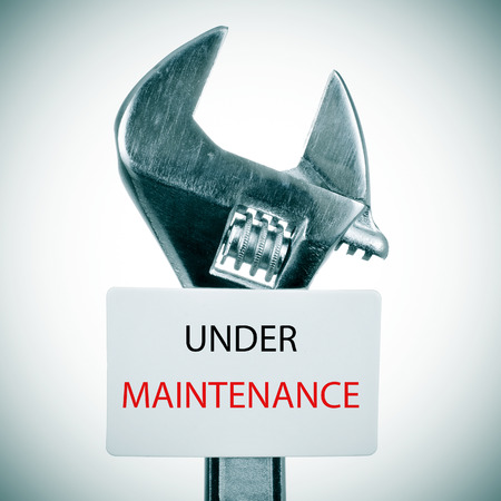closeup of an adjustable wrench and a signboard with the text under maintenance written in it, with a slight vignette addedの写真素材
