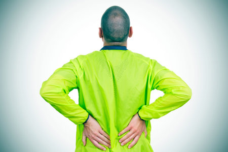 a young caucasian sportsman wearing sport clothes with his hands in his back because of his low back...