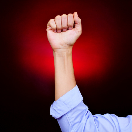 closeup of the raised fist of a young caucasian man on a black background red illuminatedの写真素材