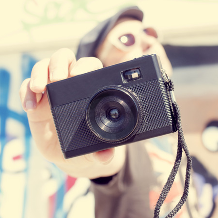 closeup of a young caucasian man wearing sunglasses and cap with a film camera in his handの写真素材