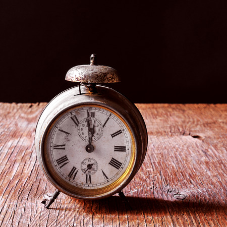 a rusty old alarm clock on a rustic wooden table, with a black backgroundの写真素材