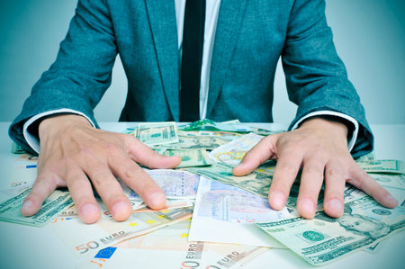 closeup of a young caucasian man in suit sitting at his office desk full of euro and dollar bills...