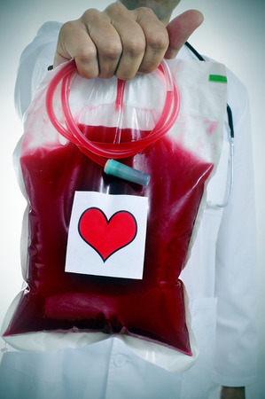 closeup of a doctor holding a blood bag with a sticker of a red heartの写真素材