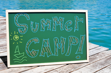 the text summer camp written with chalk of different colors in a chalkboard, on a wooden pier on the seaの写真素材