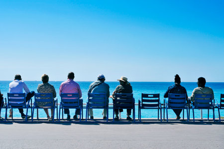 Nice, France - May 16, 2015: People sitting in the characteristic blue chairs facing the Mediterranean sea at the Promenade des Anglais in Nice, Franceのeditorial素材