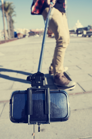 a young skater on his skateboard takes a self-portrait or a video of himself with a selfie stickの写真素材