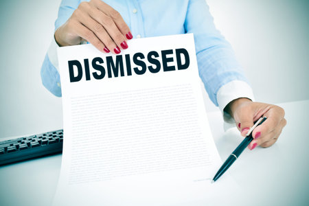 a young caucasian businesswoman sitting at his office desk shows a document with the word dismissed...