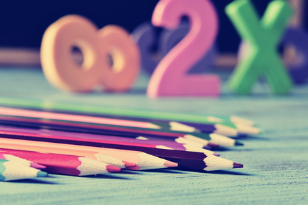 closeup of a pile of pencil crayons of different colors and some numbers on a blue rustic wooden table in a classroom, with a filter effectの写真素材
