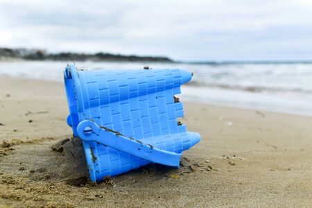 closeup of a blue toy bucket abandoned on the sand of a beach at the end of the summerの写真素材