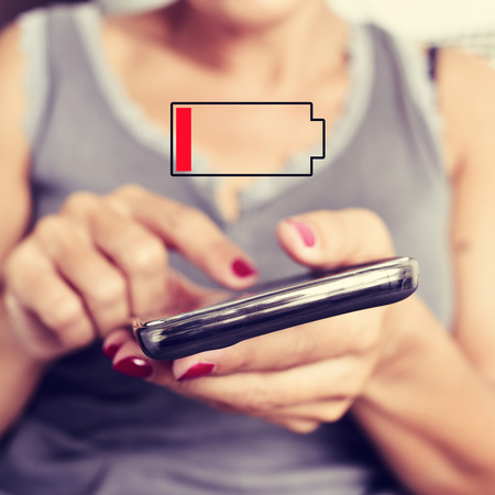 closeup of a young woman using a smartphone and an illustration of a low batteryの写真素材