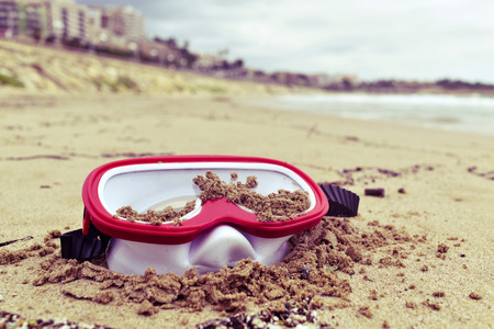 closeup of a red and white diving mask abandoned on the sand of a beach at the end of the summerの写真素材