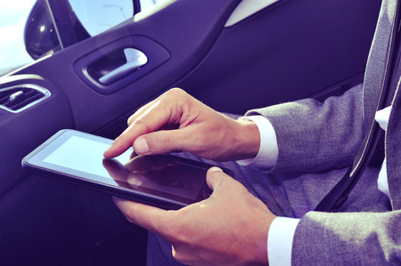 closeup of a young caucasian businessman in suit using a tablet computer in a carの写真素材