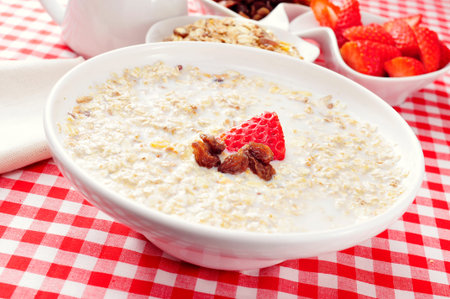 closeup of a bowl with porridge with sultana raisins and strawberry, on a set table with a checkered...