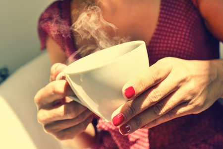 closeup of a young woman in a red dress having a cup of tea or coffeeの写真素材