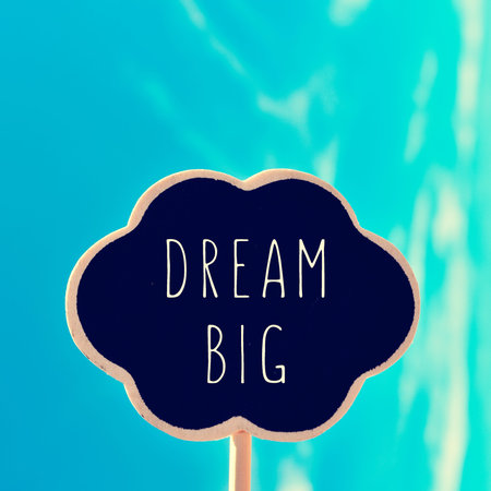 a chalkboard in the shape of a thought bubble with the text dream big, against the blue sky