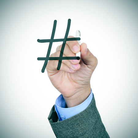 closeup of a young caucasian businessman in a grey suit handwriting a hash sign with a pen in the foreground, with a slight vignette addedの写真素材