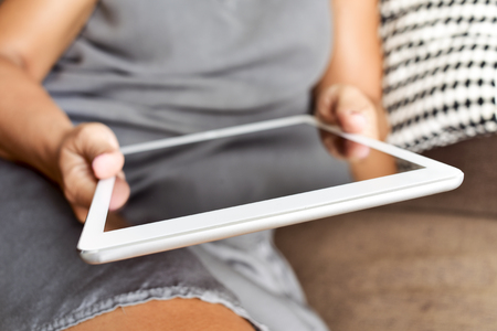 closeup of a young caucasian woman in a grey dress using a tablet in the couchの写真素材