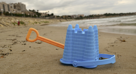 closeup of a blue toy bucket and an orange toy shovel abandoned on the sand of a beach at the end of the summerの写真素材