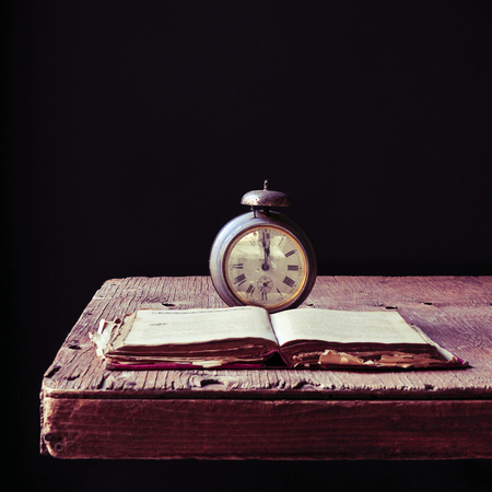 an old alarm clock and an open old book on a rustic wooden table, against a black backgroundの写真素材