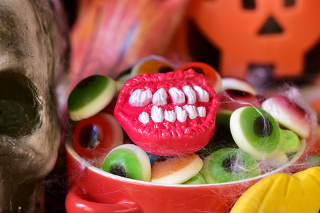 closeup of a red bowl with different Halloween candies, and some scary ornaments, such as a skull or a carved pumpkinの写真素材