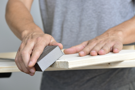 closeup of a young caucasian man sanding a wooden board with a sanding blockの写真素材