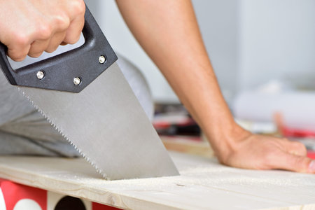 closeup of a young caucasian man sawing a wooden board with a handsawの写真素材