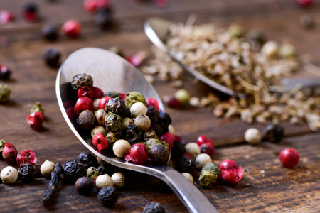 closeup of a spoon with a variety of different peppercorns, such as pink pepper, black pepper, red...