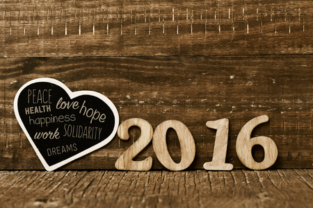 wooden numbers forming the number 2016 and a heart-shaped chalkboard with some wishes for the new year, such as peace, love and happiness, on a rustic wooden surfaceの写真素材