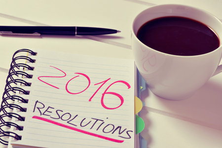 closeup of a notebook with the text 2016 resolutions written in it and a cup of coffee on a white...