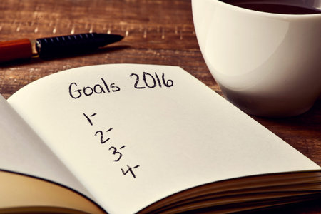 closeup of a notebook with a blank list of goals for 2016 and a cup of coffee on a rustic wooden...
