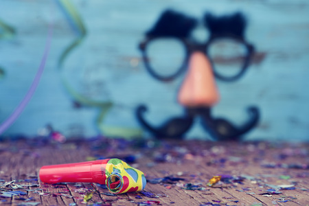 closeup of a party horns on a wooden surface full of confetti and streamers, and a pair of fake black glasses with eyebrows, a nose and a mustache forming the face of a man in the backgroundの写真素材