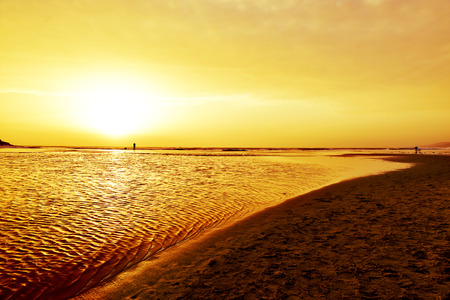 a view of the Mediterranean sea at the Lances Beach in Tarifa, Spain, at dusk, and the silhouette of a man taking a picture and a surfer in the backgroundの写真素材
