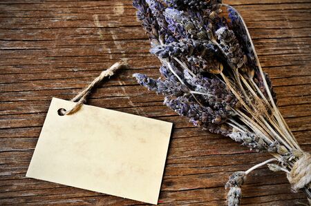 closeup of a bunch of lavender flowers tied with a string and a blank cardboard signboard on a rustic wooden surfaceの写真素材