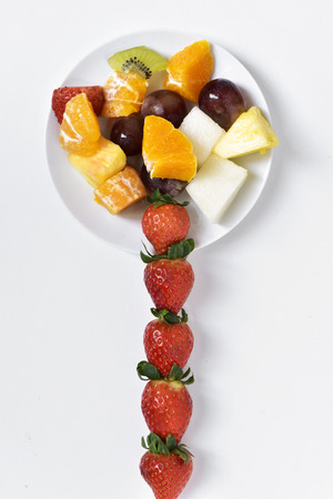 high-angle shot of a white ceramic plate with a fruit salad, made with orange, melon, kiwi, pineapple, grapes and strawberries, on a white surfaceの写真素材