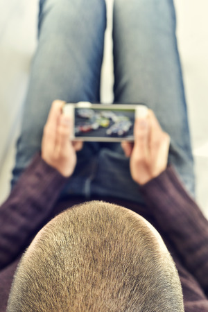 a young man lying on the couch watches a car race in streaming in his smartphoneの写真素材