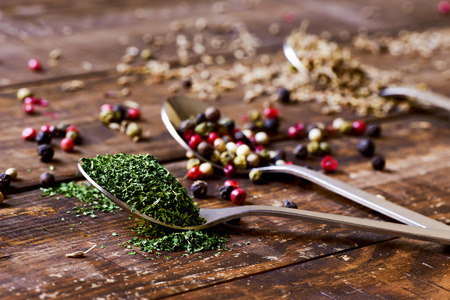 three spoons full of chopped dried parsley, peppercorns of different varieties and anise seeds on a rustic wooden tableの写真素材
