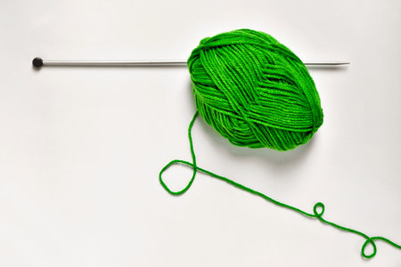 high angle shot of a ball of green yarn and a knitting pin on a white surface
