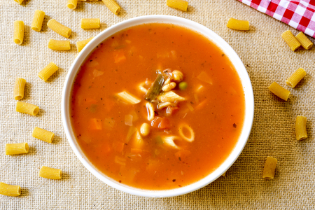 high-angle shot of a bowl with minestrone, a typical italian soup, with vegetables and pasta, on a table set with a rustic tableclothの写真素材