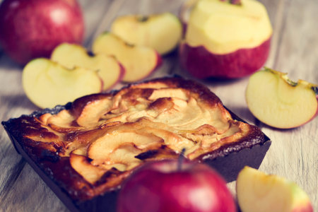 closeup of an apple cake and some red apples on a rustic wooden tableの写真素材
