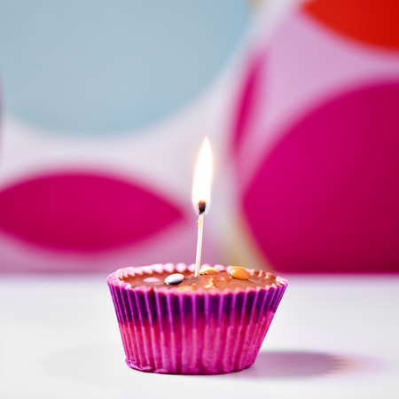 a chocolate cupcake topped with a lighted match on a white surface against a colorful geometric-patterned backgroundの写真素材
