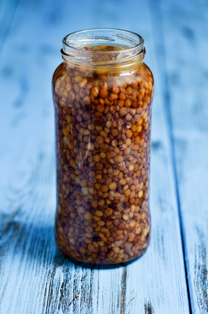 a glass jar with cooked lentils on a blue rustic wooden surfaceの写真素材
