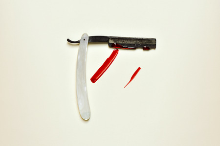 an old and rusty straight razor full of blood on an off-white backgroundの写真素材