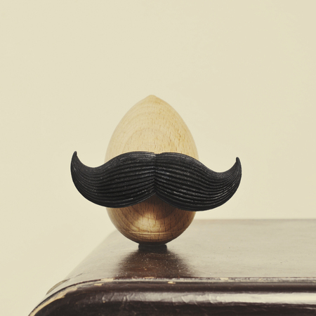 closeup of a mustached wooden egg, on an old wooden piece of furnitureの写真素材