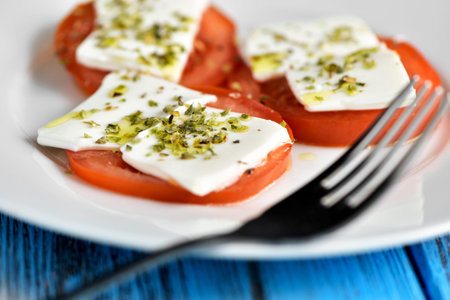 closeup of a white ceramic plate with some slices of tomato topped with fresh cheese and dressed...