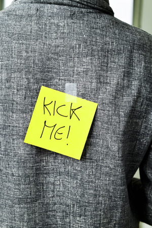 closeup of a young man with a paper with the text kick me attached to his backの写真素材